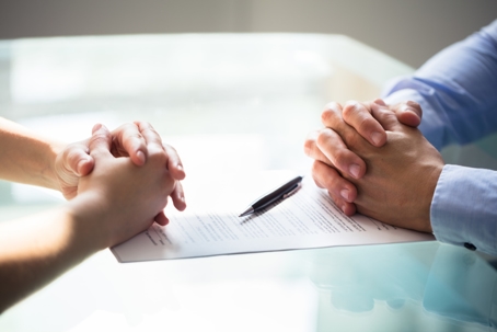 clasped hands of two people facing each other and paper and pen on table
